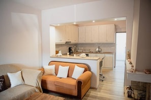 A modern living room with a sofa and a kitchen area in the background.