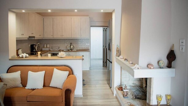 A modern kitchen with light wood cabinets, a central island, and a built-in oven.