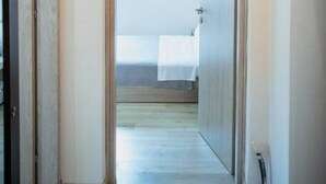A hallway leading to a bedroom with a bed, a door on the left, and a light switch on the wall.