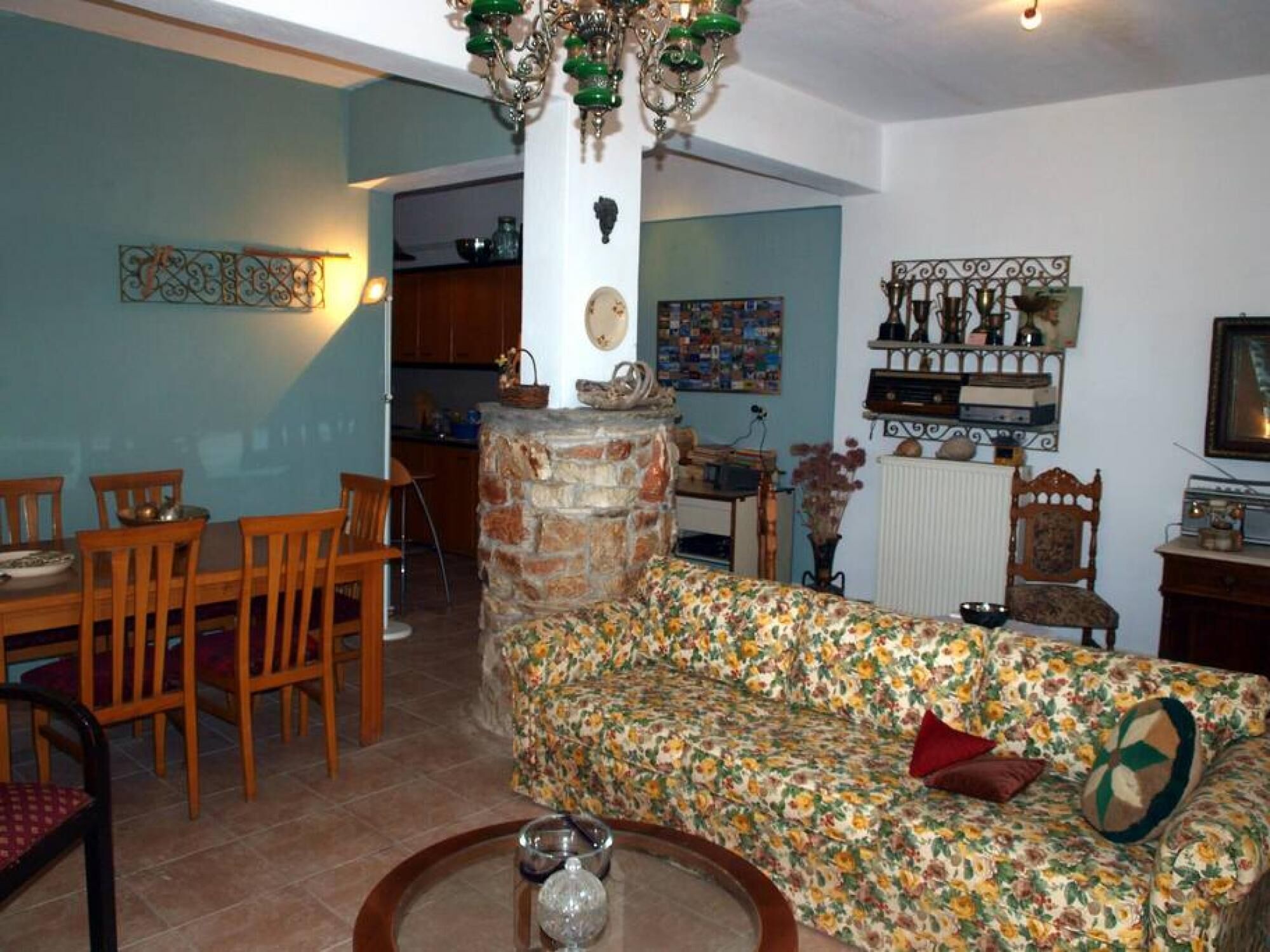 Uma sala de estar com lareira de pedra, sofá floral, mesa de jantar de madeira e cadeiras.