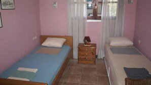 A bedroom with two single beds, a wooden dresser, a window with curtains, and a small table with a decorative item.
