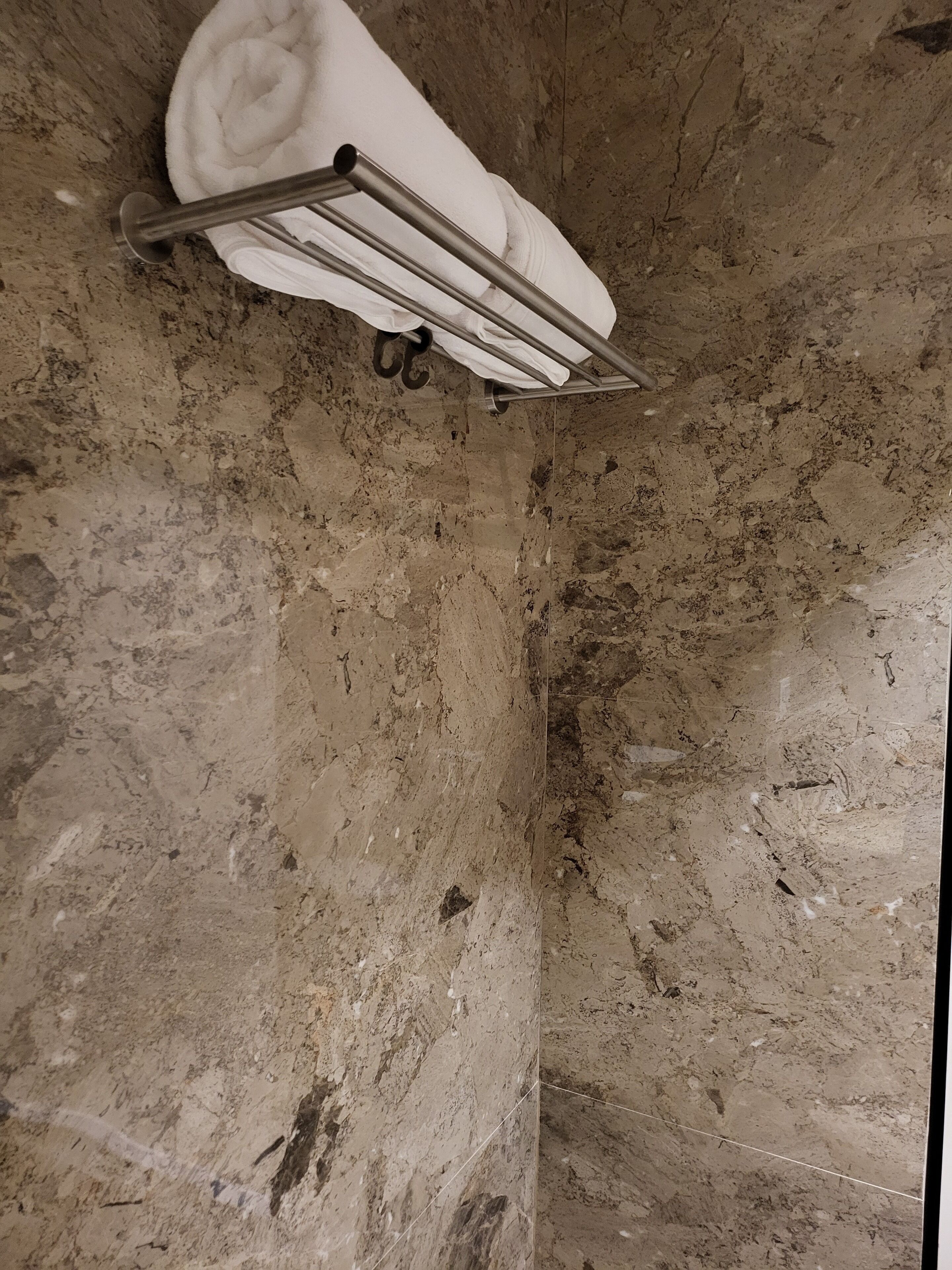 Un baño con un perchero que sostiene una toalla doblada, un perchero metálico y una pared de piedra texturizada.