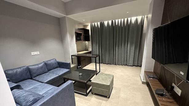 Una sala de estar moderna con un sofá gris, una mesa de centro, un televisor y una cocina al fondo.