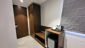 Ein kompaktes Hotelzimmer mit Küchenzeile, einem kleinen Kühlschrank und einer Sitzecke mit einer Bank.