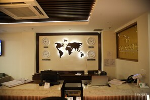 A reception desk with a world map and clocks indicating time in Delhi, Tokyo, New York, and Singapore. - Belvedere Suites- A Boutique Business Expo Hotel (Greater Noida)