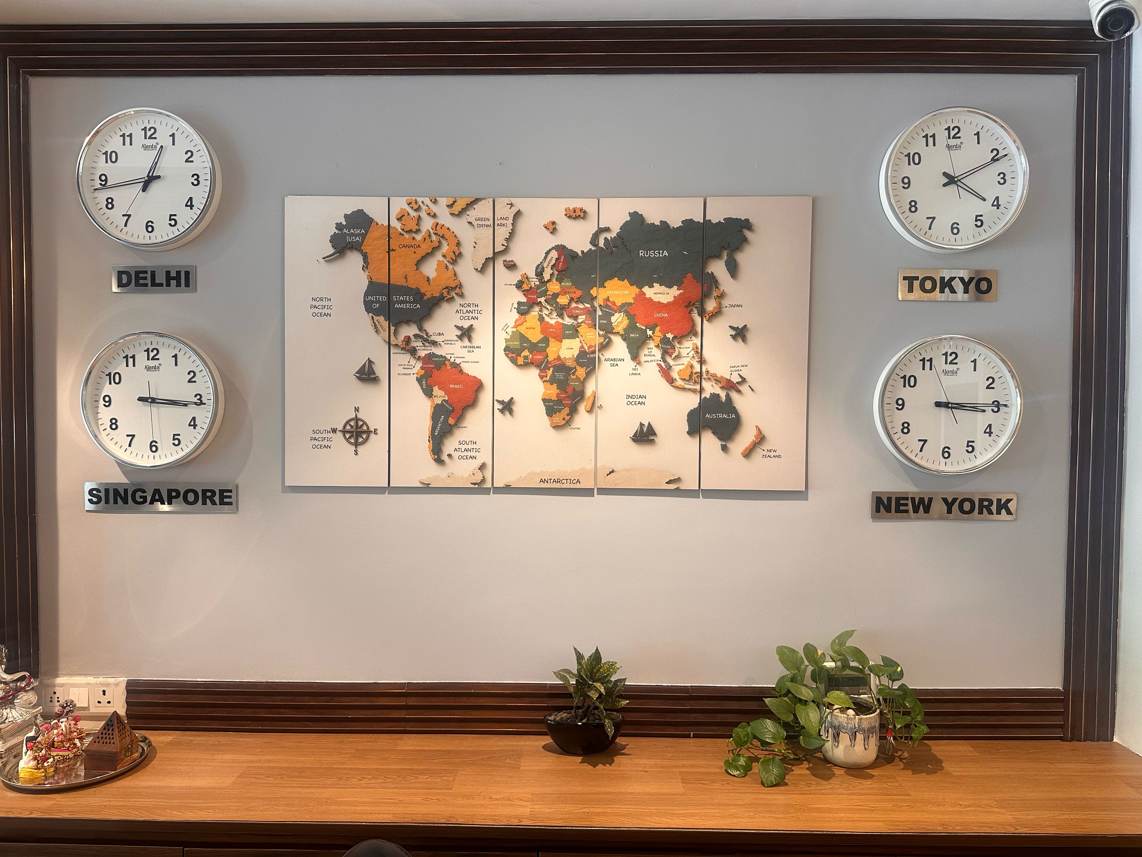 Uma parede com quatro relógios, cada um mostrando a hora de uma cidade diferente: Delhi, Singapura, Tóquio e Nova Iorque.