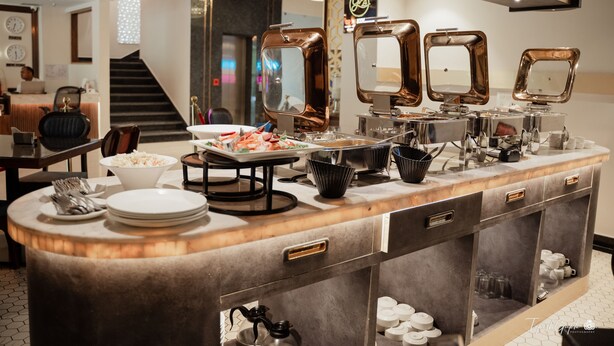 En buffetopstilling med flere serveringsstationer, en trappe og et siddeområde med borde og stole.