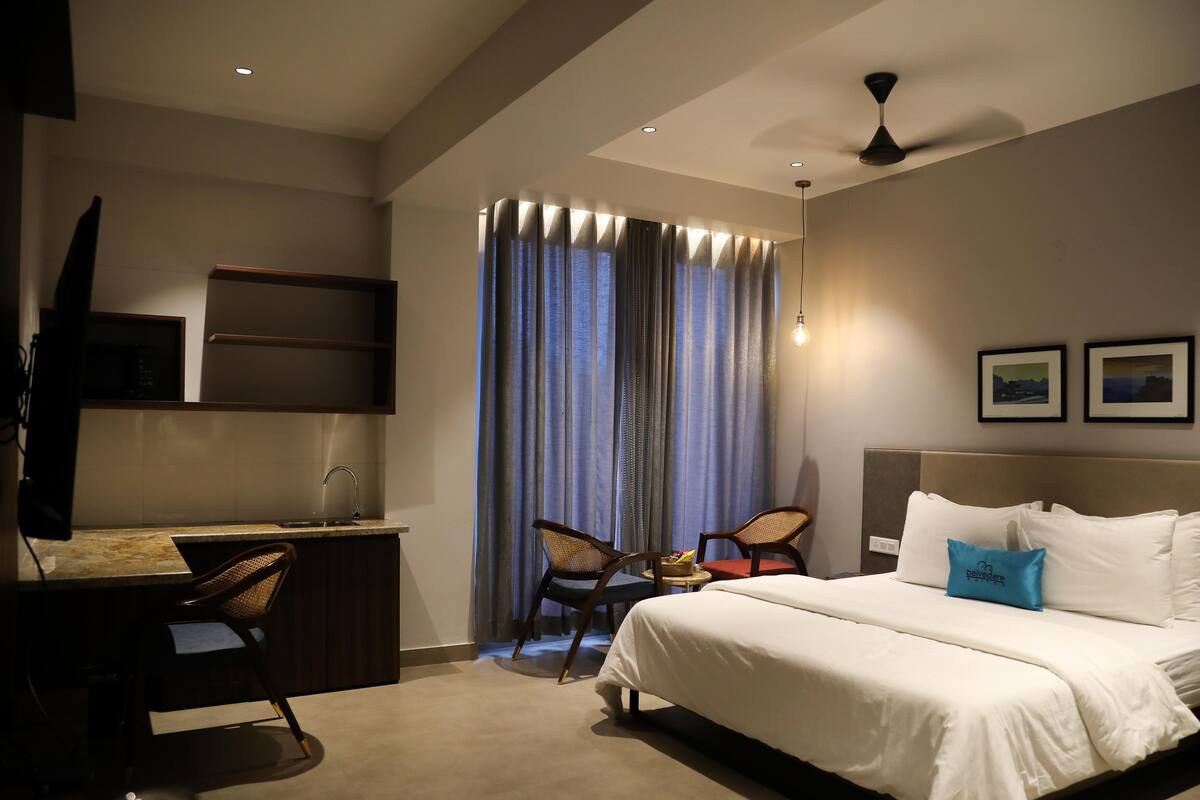 A hotel room with a bed, desk, chairs, a TV, and curtains.