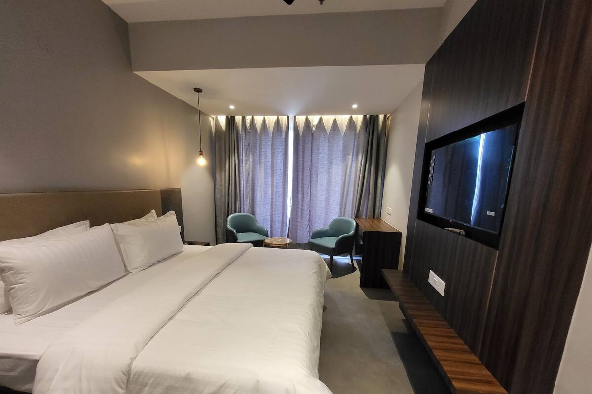A hotel room with a large bed, a desk, two chairs, a TV, and curtains.
