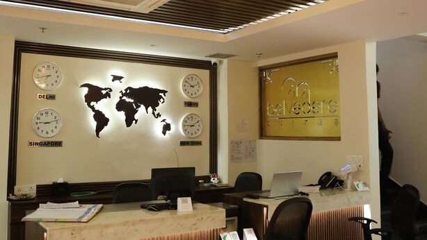 A modern office with a world map and clocks indicating different cities, a wooden ceiling with hanging lights, and a reception desk with computers and chairs. - Belvedere Suites- A Boutique Business Expo Hotel (Greater Noida)