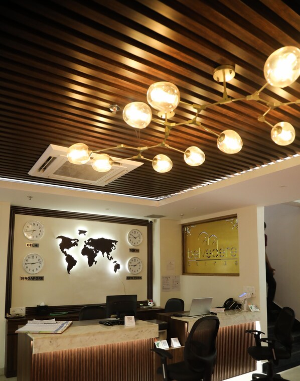 A modern office with a world map and clocks indicating different cities, a wooden ceiling with hanging lights, and a reception desk with computers and chairs.