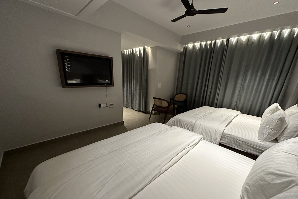 A hotel room with two beds, a TV mounted on the wall, a ceiling fan, and a chair.