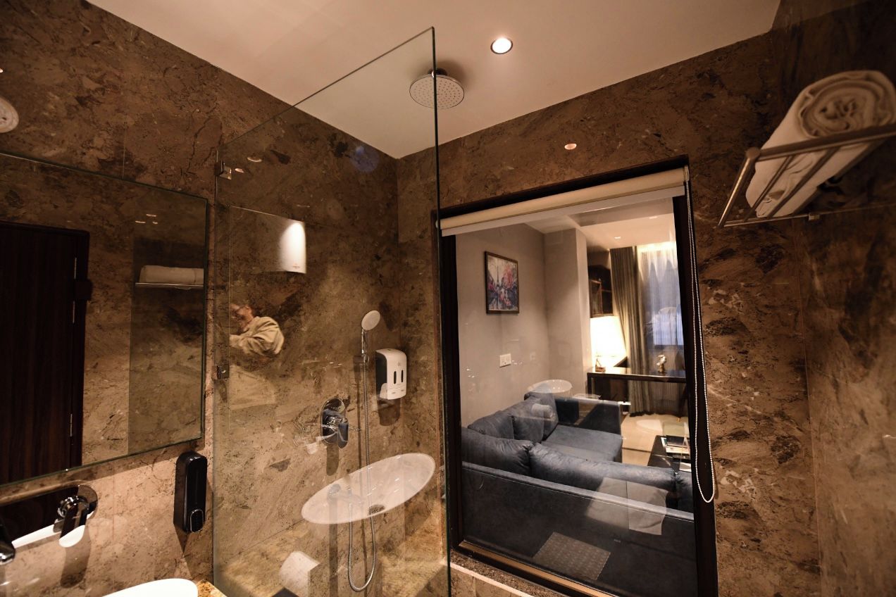 Un baño moderno con cabina de ducha de vidrio, pared de mármol, lavamanos y espejo.