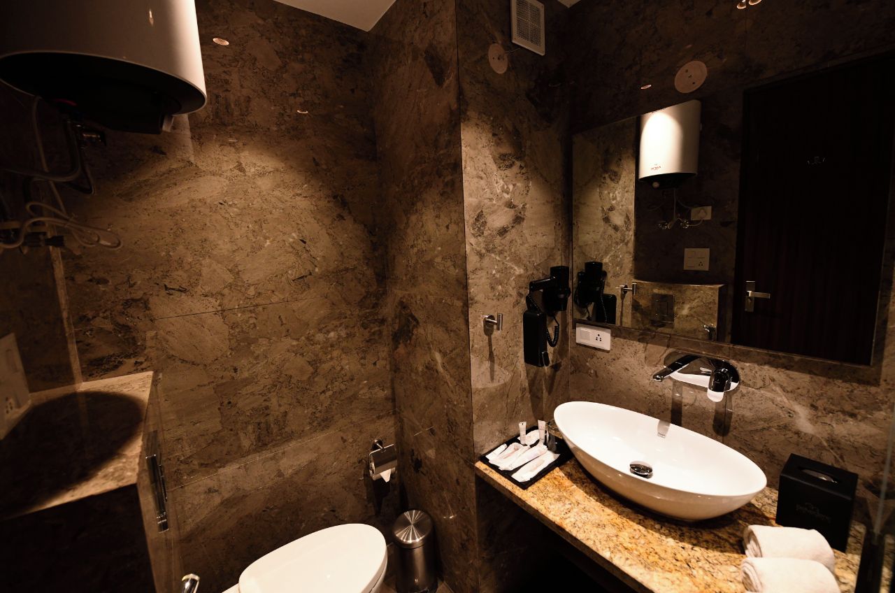 Un baño con pared de mármol, un lavamanos, un espejo y un dispensador de toallas.