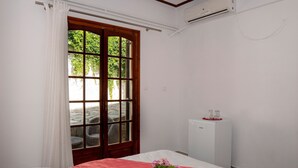 A hotel room with a bed, a window with curtains, a small white cabinet, and a radiator. - Paradeisos Double Room 6 (Zagora-Mouresi)