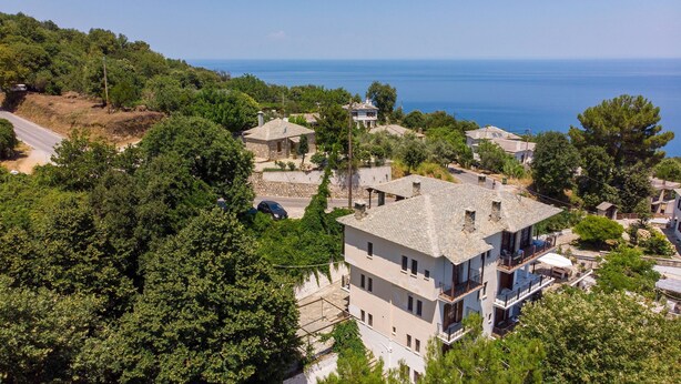A coastal residential area with stone buildings, a paved road, and a view of the sea. - Paradeisos Double Room 6 (Zagora-Mouresi)