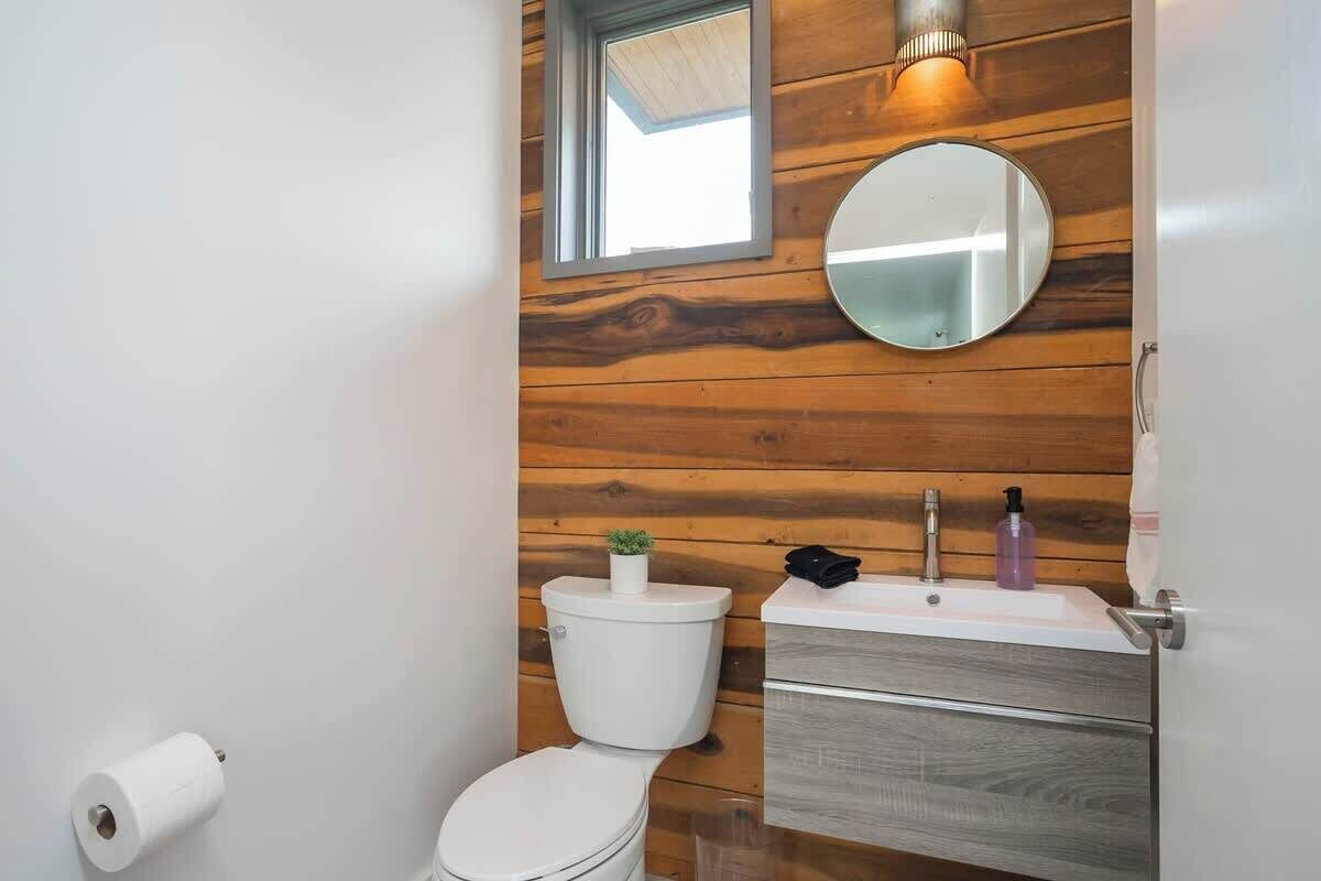 Ein Badezimmer mit Holzverkleidung, einer Toilette, einem Waschbecken mit Spiegel und einem kleinen Fenster über der Toilette.