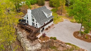 A large white house with a steep roof, a deck, and a stone staircase leading to a porch.