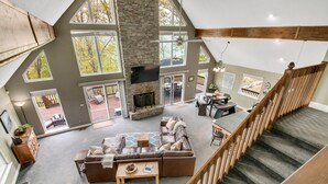 A spacious living area with a stone fireplace, large windows, and a wooden staircase.