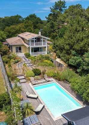 Una casa a due piani con piscina, circondata da vegetazione lussureggiante e un pontile in legno.