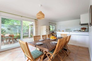 Cucina e zona pranzo open space con tavolo in legno imbandito per sei persone, lampadario a sospensione e vista attraverso le porte in vetro.