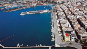 An aerial view of a coastal city with a marina, dense urban buildings, and a clear blue harbor. - Casa Anna Maria in Volos (Volos)