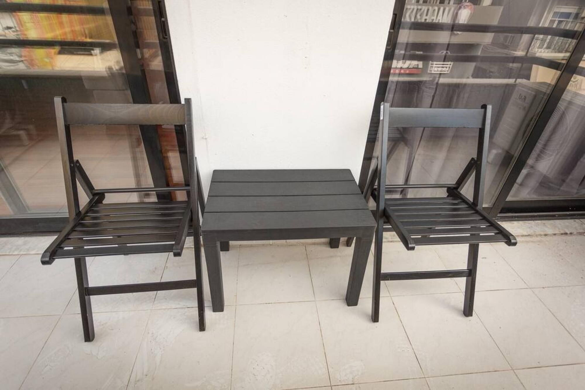 A small, dark-colored table with two matching chairs in front of a white wall.