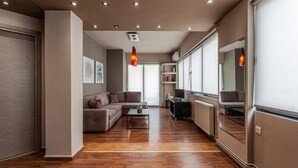 A modern living room with a sectional sofa, a coffee table, and a TV. There are ceiling lights and a large window providing natural light. - Casa Anna Maria in Volos (Volos)