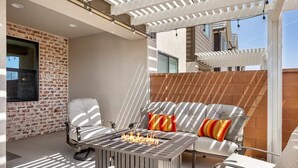 Eine Terrasse im Freien mit Feuerstelle, Sitzgelegenheiten und einer Pergola.