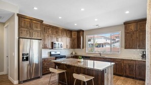 Una cocina moderna con armarios de madera, electrodomésticos de acero inoxidable, una isla grande con taburetes y un ventanal con vistas al exterior.