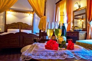 Quarto de hotel com uma cama, dois copos de vinho e uma mesa com toalha rendada e rosas.