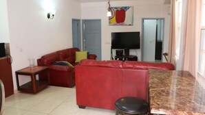 Un salon avec un canapé rouge, une petite table, un téléviseur et un tableau accroché au mur.