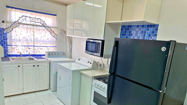 Une cuisine avec des meubles blancs, un réfrigérateur noir, un four à micro-ondes, une cuisinière et un lave-linge.