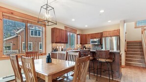 A modern kitchen with wooden cabinets, stainless steel appliances, and a dining area with wooden chairs and a table. - Stunning 3 BR Townhome in Keystone! Enjoy the complex hot tub after a long day o (Keystone)