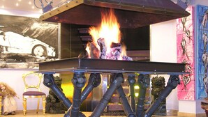 Ein modernes Interieur mit einem zentralen Kamin, einem Gemälde eines Oldtimers und abstrakter Kunst an den Wänden.