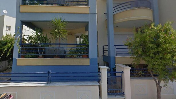 A multi-story building with balconies, a palm tree, and a gate.
