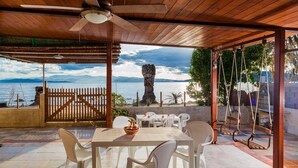 Un espacio al aire libre cubierto con mesa y sillas, un conjunto de columpios y vistas al mar y las montañas.