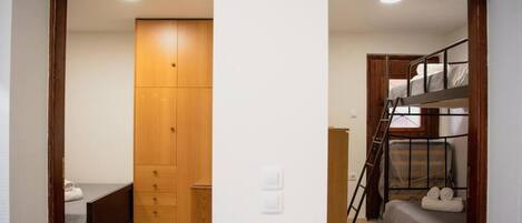 A bedroom with a wooden wardrobe, a bed, and a bunk bed.
