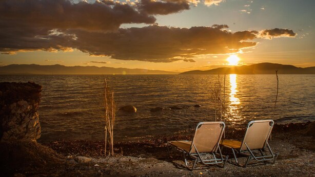 Una vista del atardecer sobre una masa de agua, con dos sillas de playa mirando hacia la orilla.