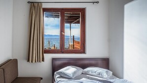 Un dormitorio con cama, ventana con vista al mar y un sofá marrón.