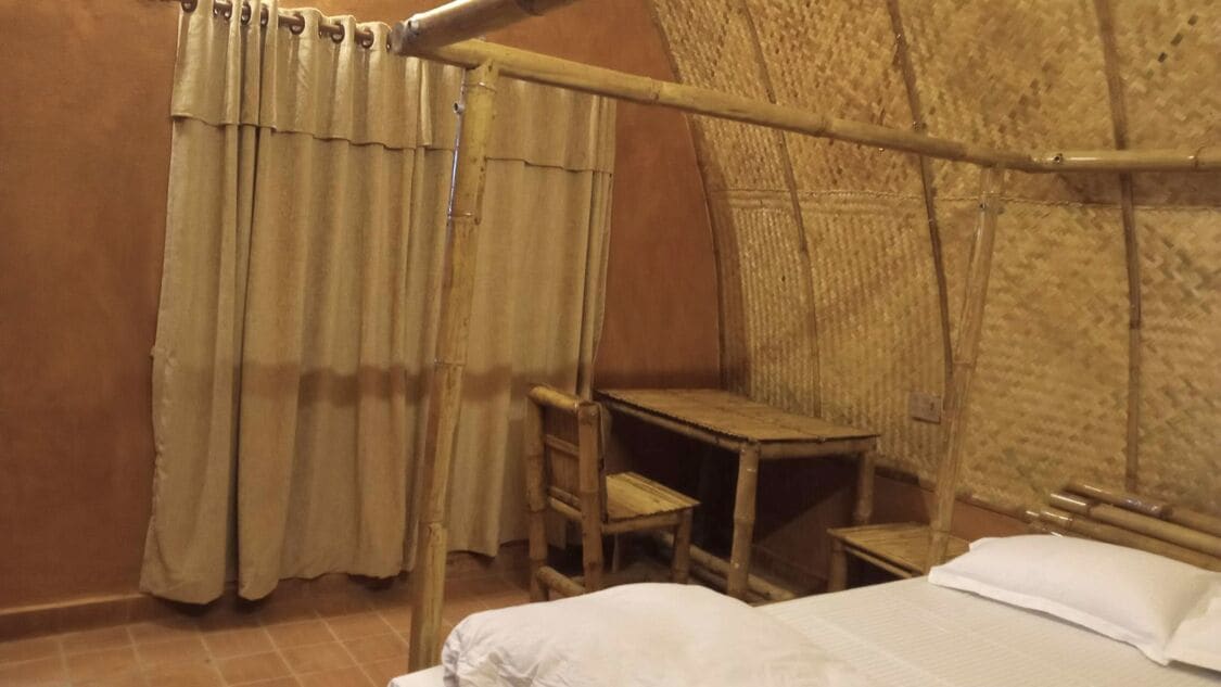 A room with a bed, a small wooden table, a chair, and a curtain.