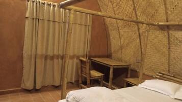 A room with a bed, a small wooden table, a chair, and a curtain.