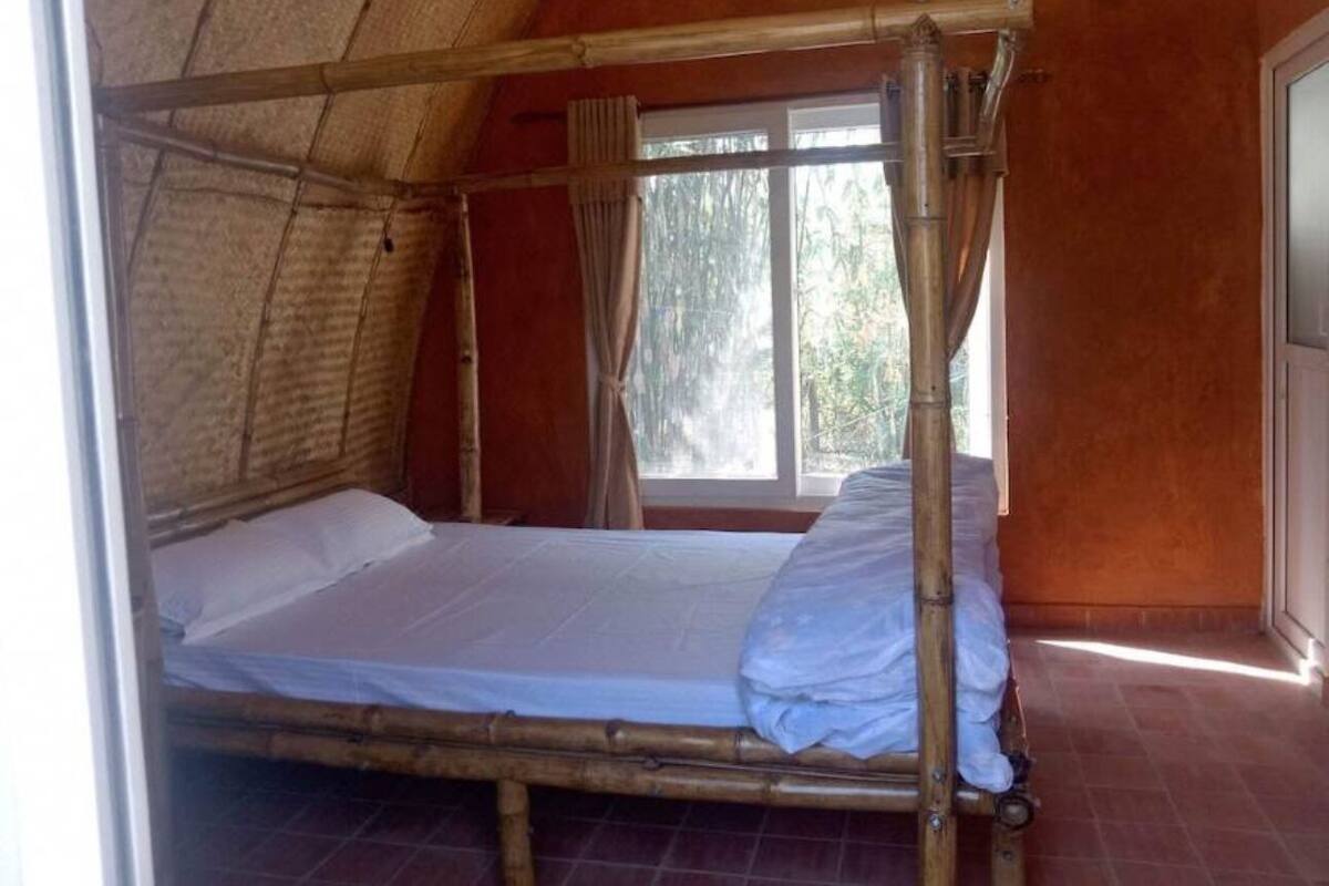 Una cama individual con estructura de bambú en una habitación con techo inclinado y ventana.