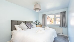 A bedroom with a bed, a nightstand, a window with curtains, and a chandelier.