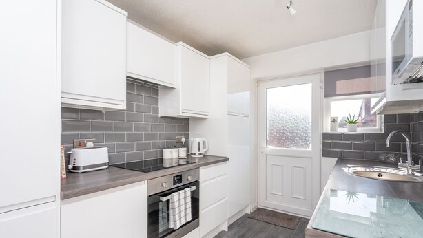 A modern kitchen with white cabinets, a stainless steel oven, and a grey tiled backsplash.