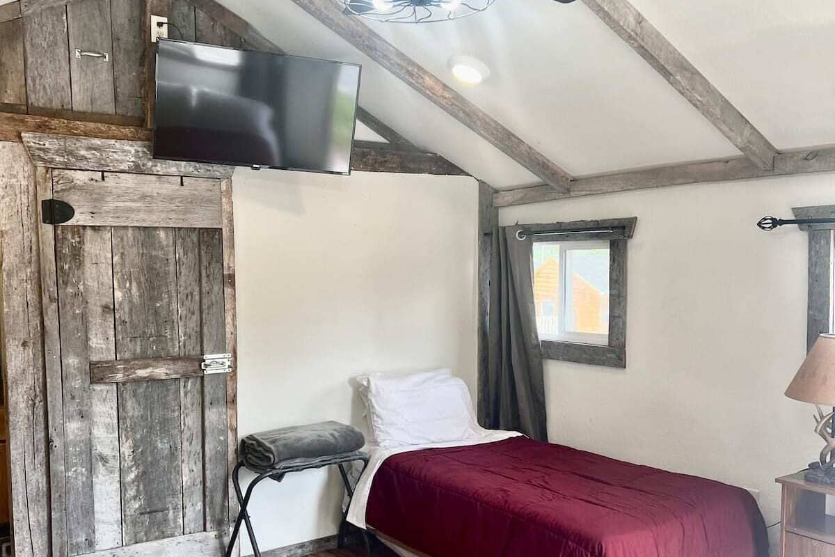A room with two beds, a ceiling fan, a TV, and a rustic wooden door.
