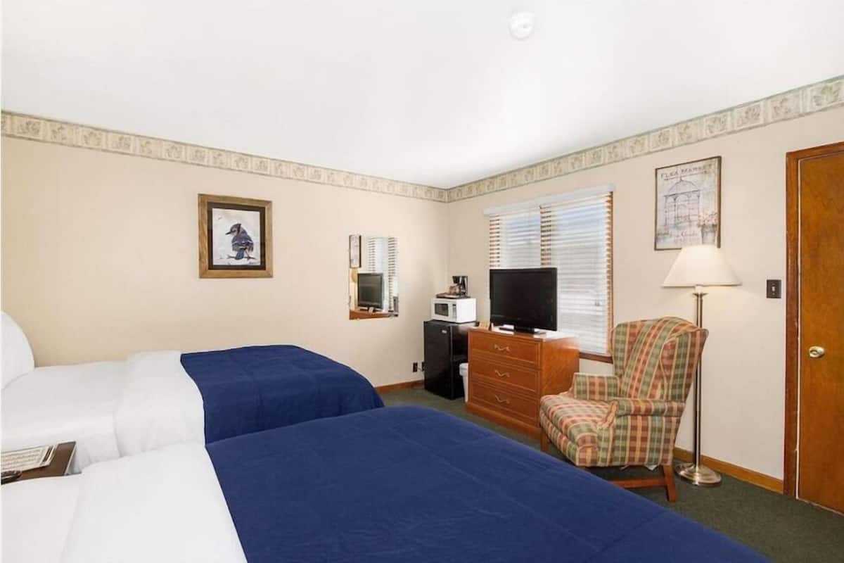 A hotel room with two beds, a television, a desk with a computer, a chair, and a lamp.