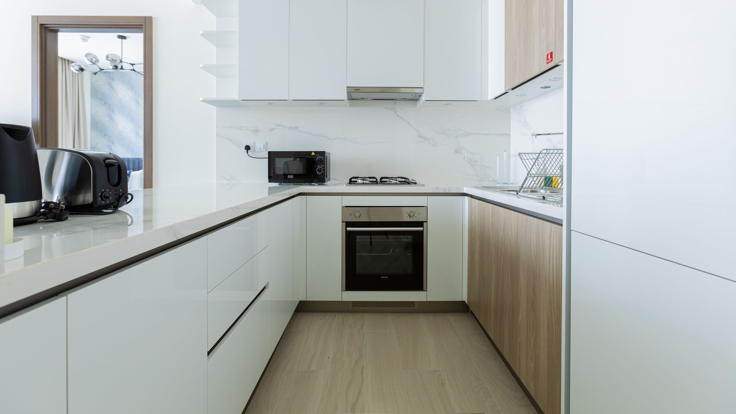 Una cocina moderna con armarios blancos, horno empotrado, microondas y tostadora.