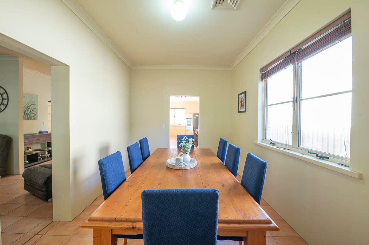 A dining area with a wooden table, blue chairs, a vase with flowers, and a window with blinds.