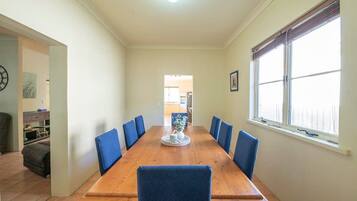 A dining area with a wooden table, blue chairs, a vase with flowers, and a window with blinds.